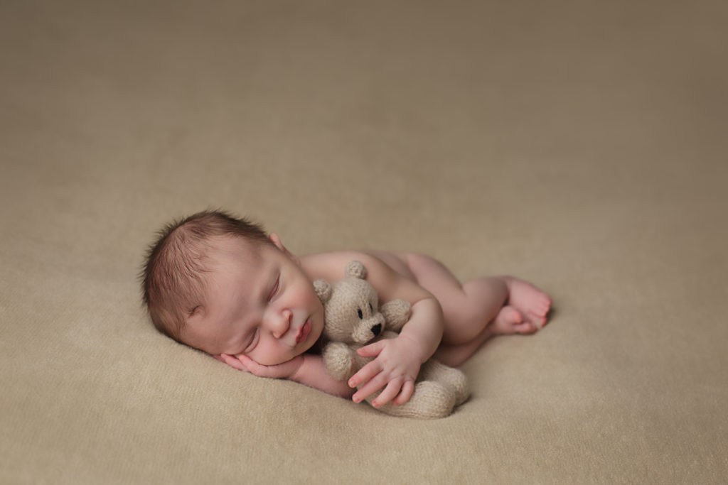 Baby boy posed for his newborn portraits holding a little teddy bear.